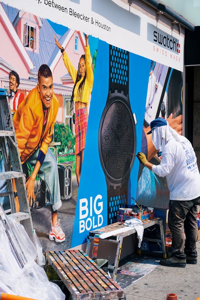 get-in-touch A street artist creates a vibrant mural in an urban setting near Swatch store.